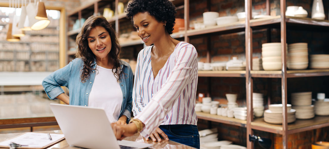 Dos mujeres trabajadoras en un local de cerámica señalando un detalle en el portátil