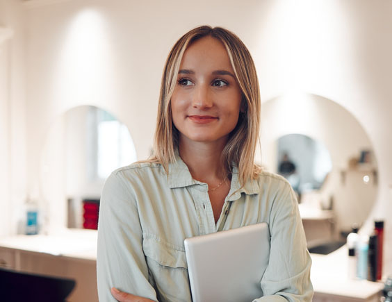 Chica joven en una peluquería abrazando una tablet y con cara emocionada