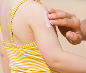 Persona echando crema sobre el brazo de una niña